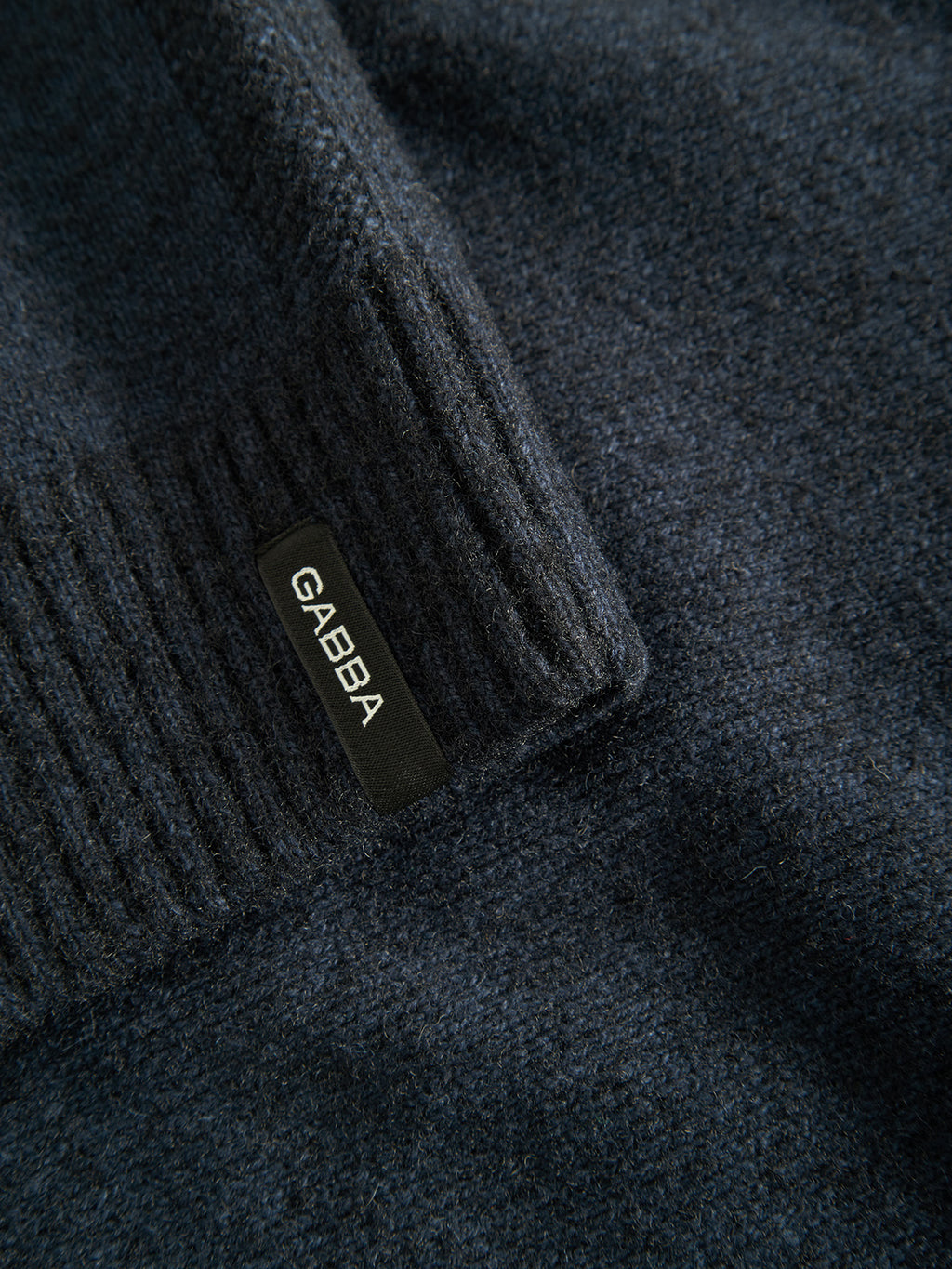 Close-up of dark blue textured fabric, possibly from the Gabba Luca Ls - Navy sweater. The ribbed section includes a small black label reading GABBA. Crafted from mixed regular wool, the material looks soft with a slightly woolly texture.