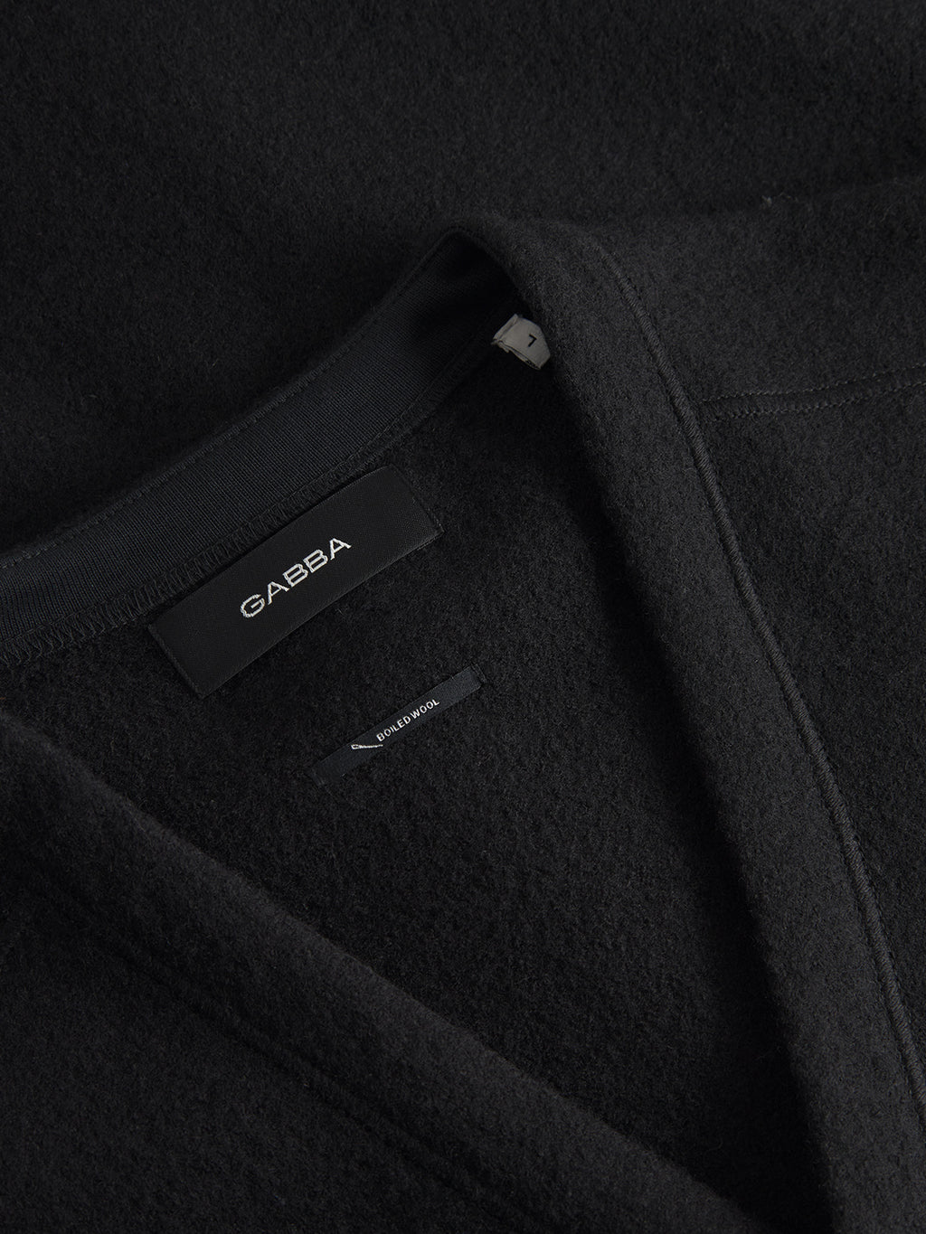Close-up of a black garment, Mattia Ls - Meteorite by Gabba, featuring a V-neckline crafted from soft, textured boiled wool. The label reads Gabba Wellington, emphasizing its premium quality.
