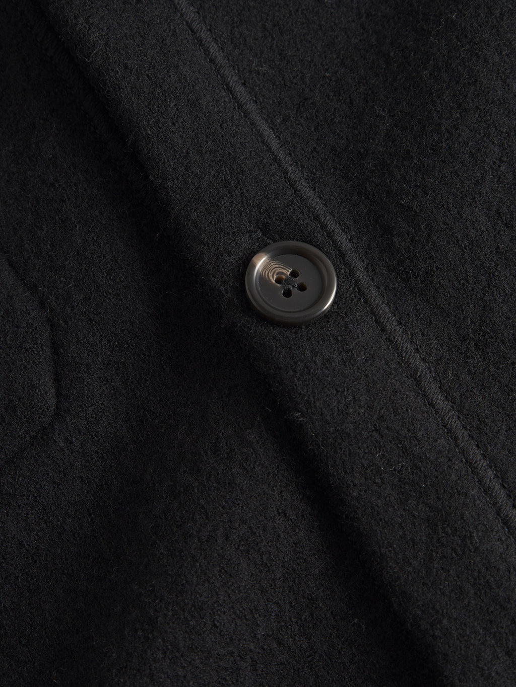 Close-up of the Gabba Mattia Ls - Meteorite coat in black boiled wool, featuring a smooth texture. A single dark button reflects light and detailed stitching around it enhances its classic cardigan style design.
