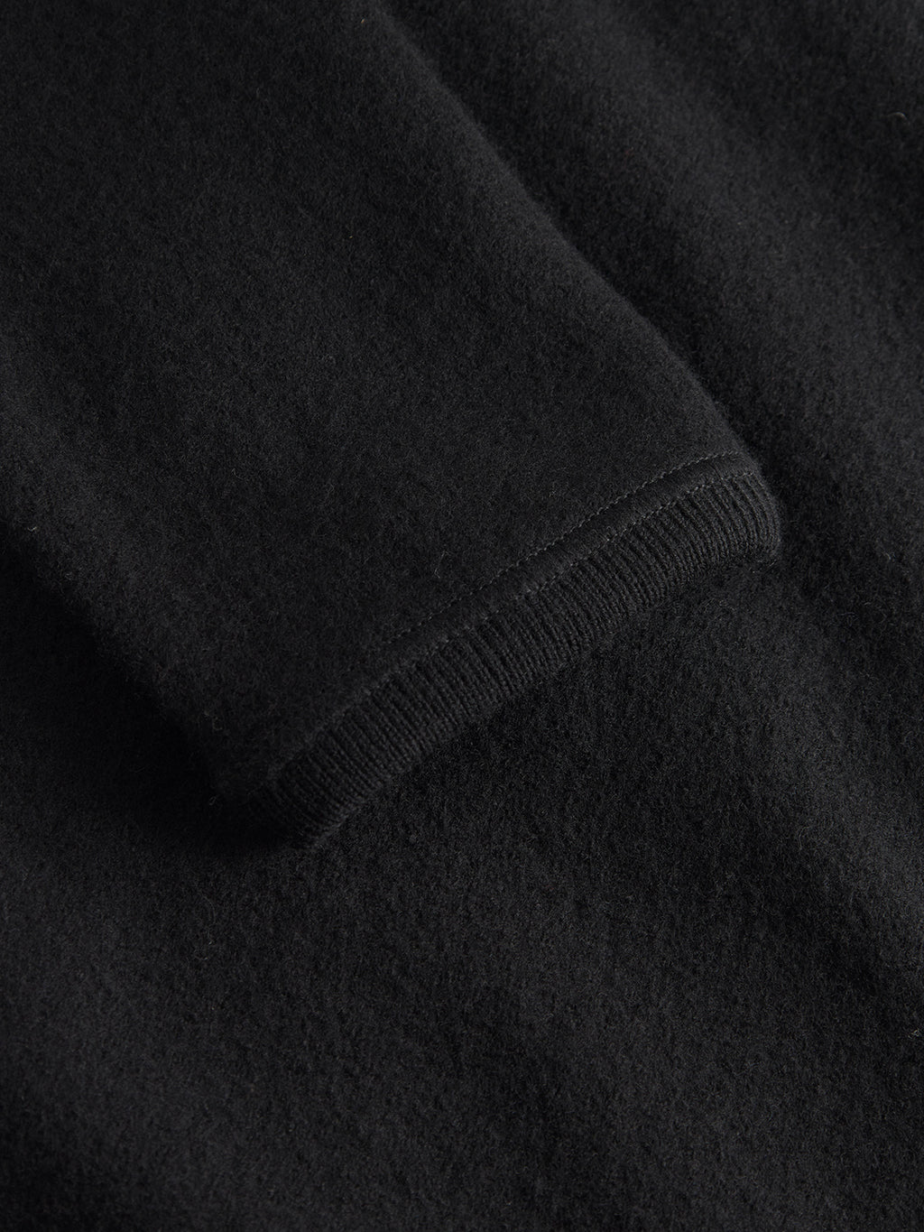 A close-up of the Gabba Mattia Ls - Meteorite black fabric sleeve highlights its soft, smooth texture with a neatly hemmed edge. The lighting emphasizes the rich, even color of this exquisite material.