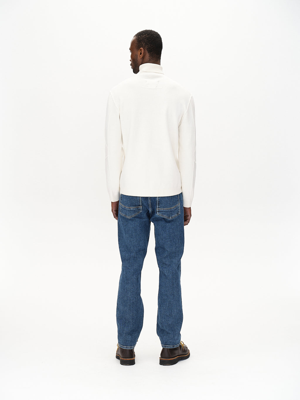 Against a plain white backdrop, a person in blue jeans showcases their style by wearing Gabbas Blanko High Ls - Off White sweater, standing with their back to the camera.