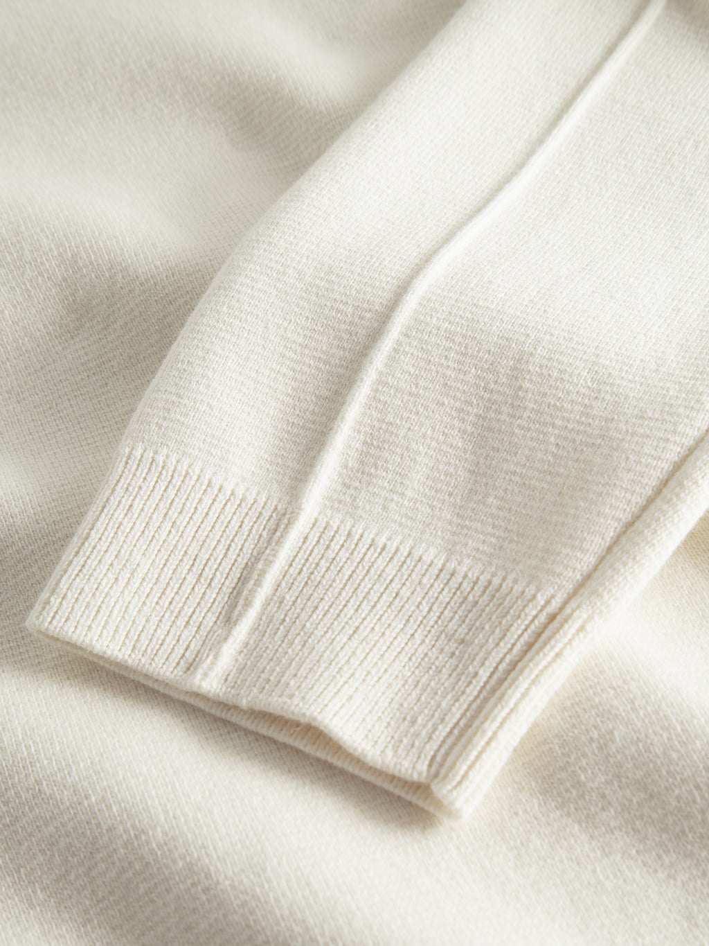 The Gabba Blanko High Ls sweater in off-white Milano knit features textured, ribbed cuffs and sleeves. Showcased lying flat on a matching fabric background, its soft and cozy material highlights the garment’s quality, making it a timeless addition to any stylish wardrobe.