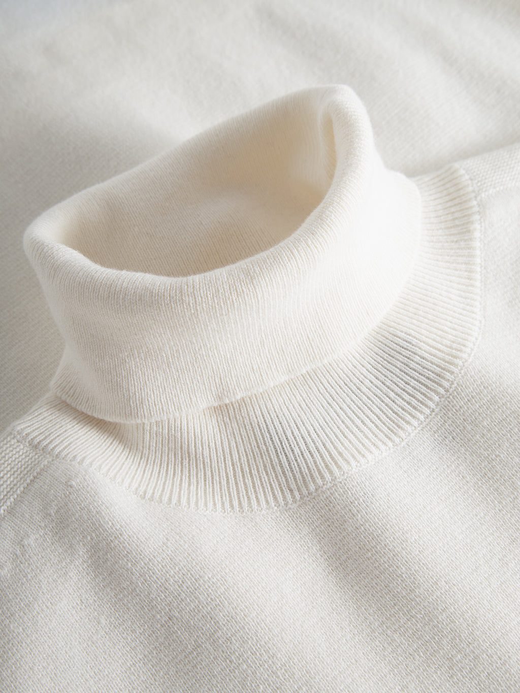 A close-up of Gabbas Blanko High Ls in off white, crafted in Milano knit, highlights its soft ribbed texture. The cozy fabric and smooth turtleneck fold make it an essential piece for any stylish wardrobe.