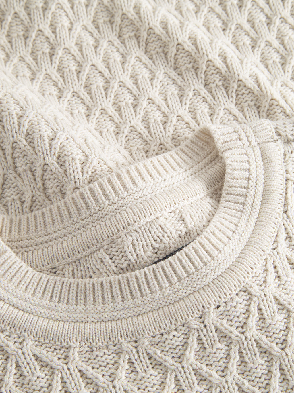 Close-up of the Gabba Aksla Ls - Egret sweater in cream, highlighting its honeycomb and diamond knit pattern. Neatly folded to reveal its ribbed neckline and intricate stitching, it is expertly crafted from 100% cotton for exceptional comfort.
