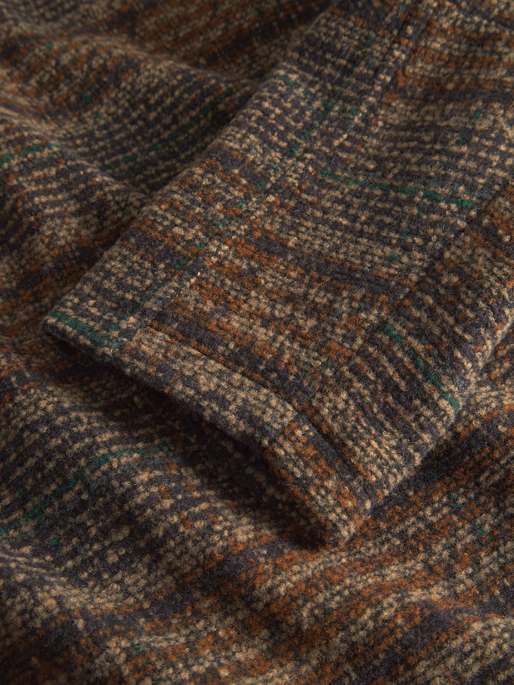 The Oscar J Check by Gabba showcases a close-up of folded fabric in earthy tones of brown, orange, green, and navy blue. Its soft, woolly texture resembles a cozy wool blend jacket that promises warmth and comfort.
