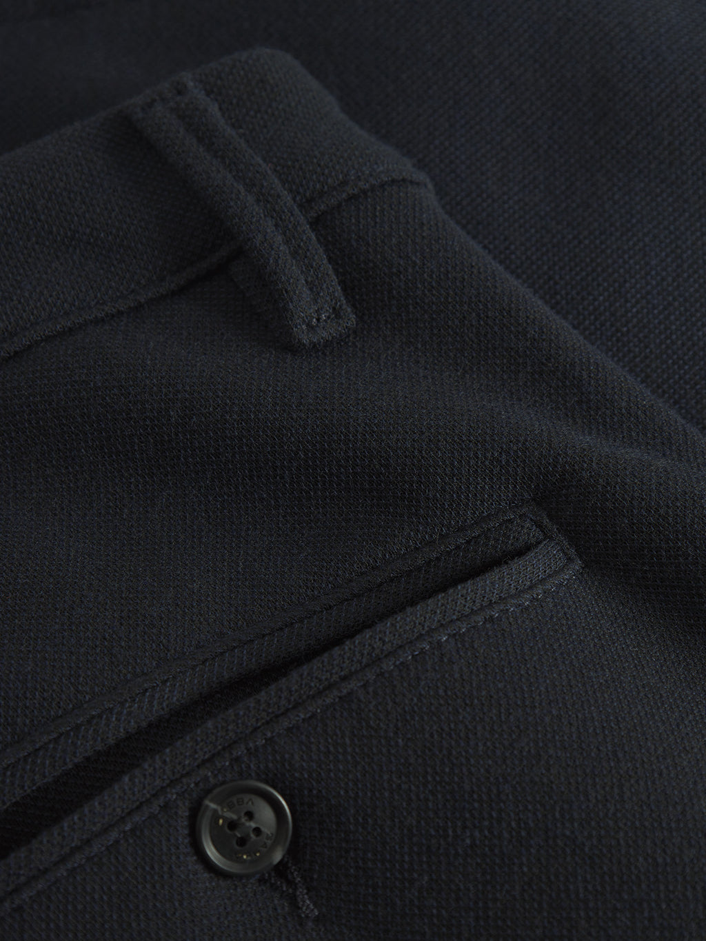 Close-up of navy fabric from Gabbas Paul GKnit pants, showcasing a pocket with stitching, a belt loop, and a black button. The smooth, tightly woven texture highlights the unique knitting technique.