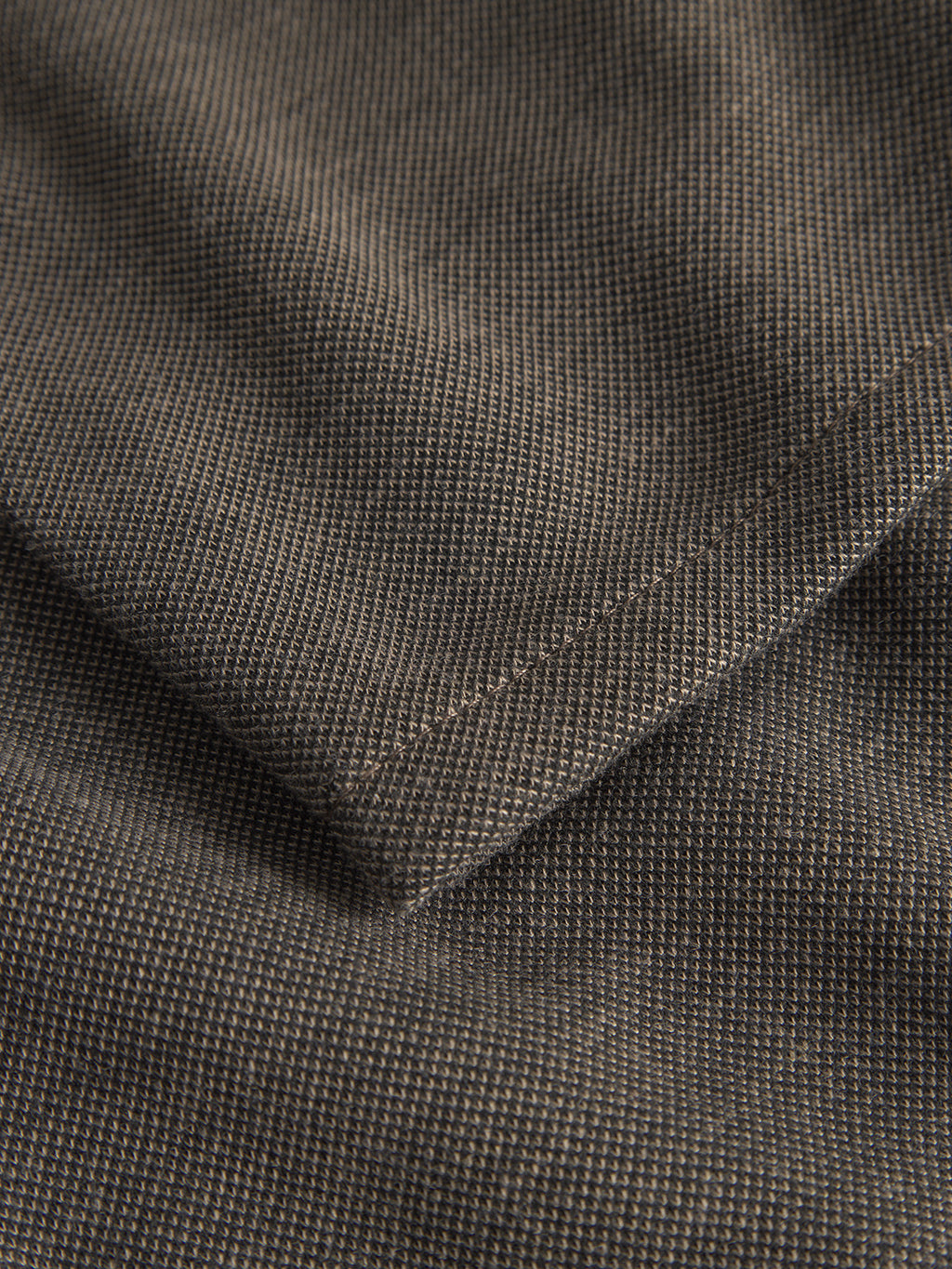 Close-up of a folded piece of dark gray textured fabric with a subtle grid pattern, perfect for Gabbas Paul GKnit - Sand pants. The material looks slightly rough, with visible weaves and stitches creating a checkered effect. The lighting enhances the fabrics texture and form.