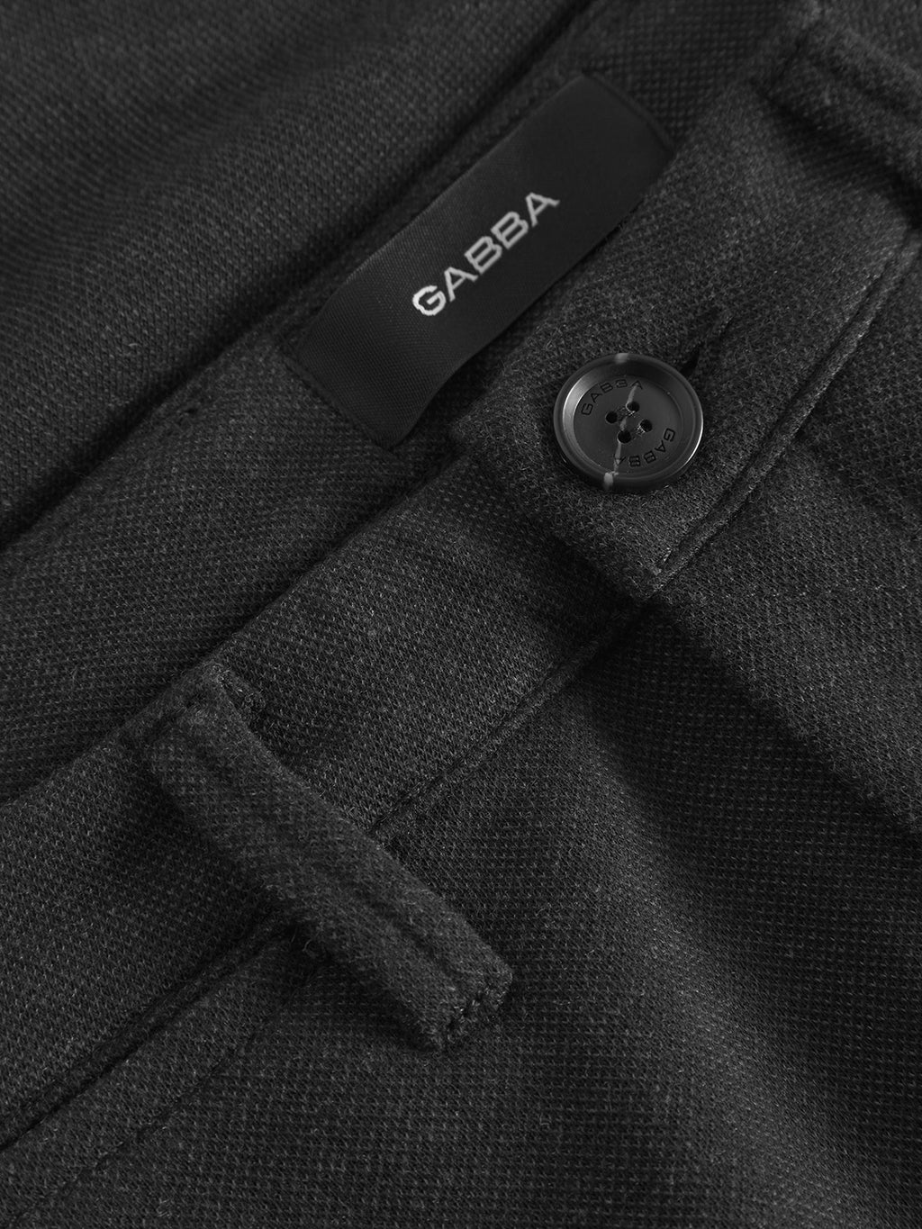 Close-up of dark grey textured Paul GKnit pants by Gabba with a button and a label. The fabric displays a subtle weave pattern for everyday wear, with the slim fit accentuated by the button near a belt loop.