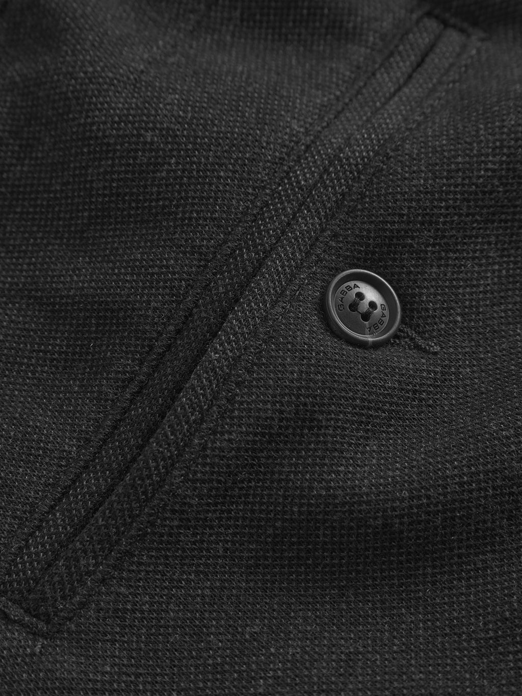 Close-up of the dark grey Paul GKnit fabric by Gabba, featuring a button engraved with Born and Raised. The slim fit design has a stitched seam leading to the button, forming a subtle line perfect for everyday wear.