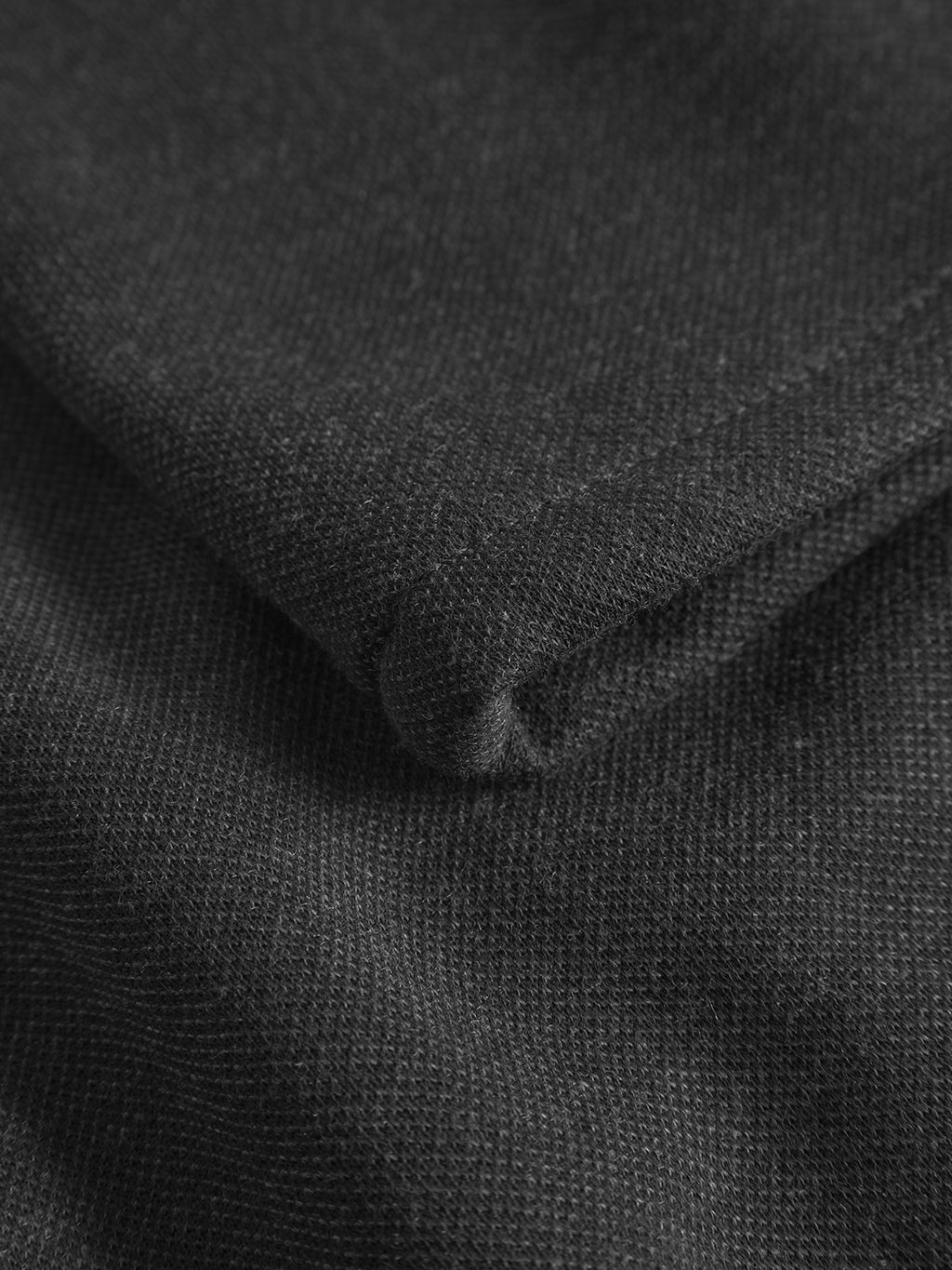A close-up of folded dark grey fabric from Gabbas Paul GKnit reveals a fine, even weave. The texture, highlighted by light, indicates soft durability, ideal for Gknit pants made for everyday use.