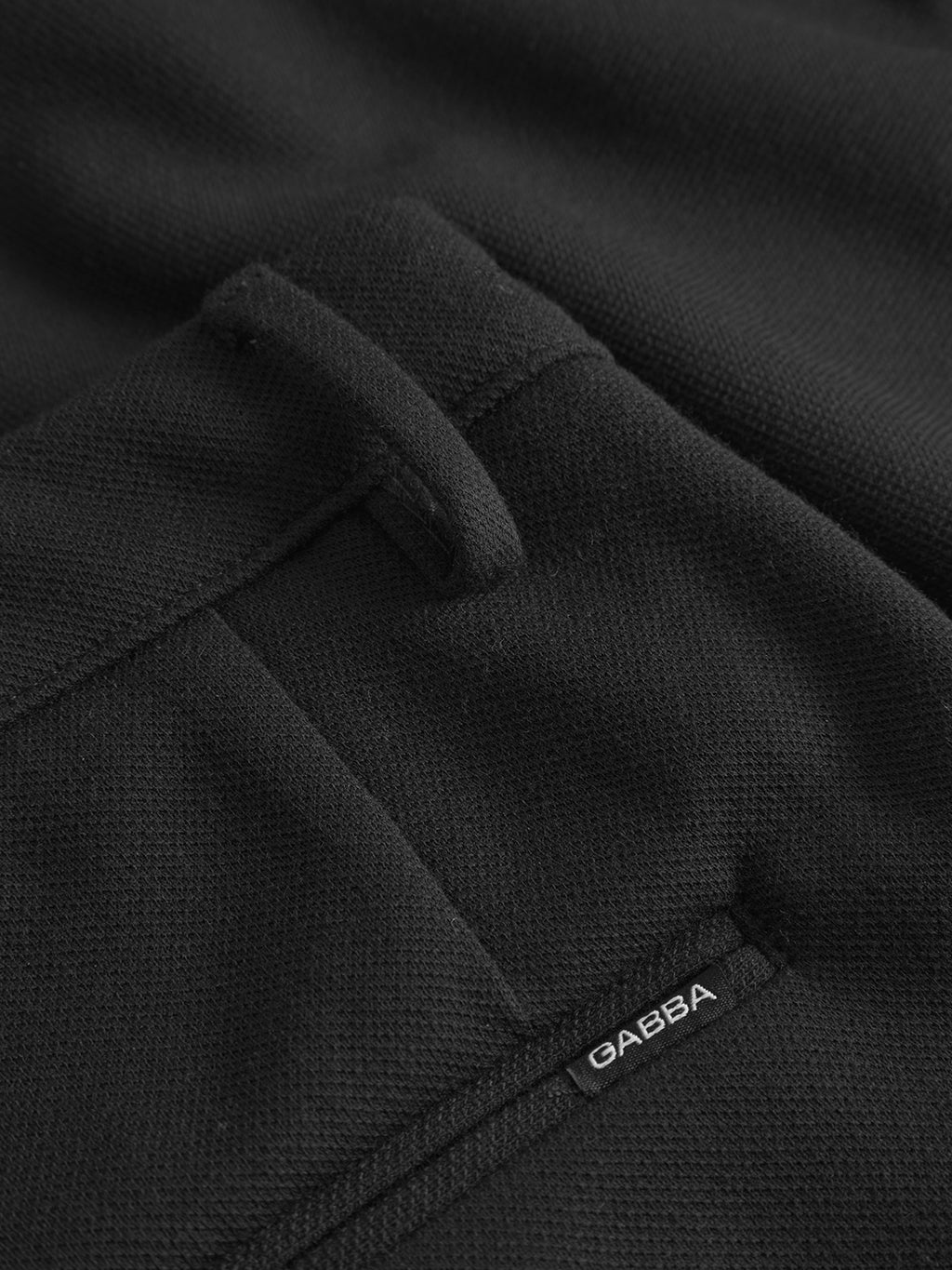 Close-up of the textured black fabric showing a pocket with a white Gabba label. The Verona GKnit - Meteorite pants have belt loops, subtle stitching, and a loosely fit design crafted from structured fabric.