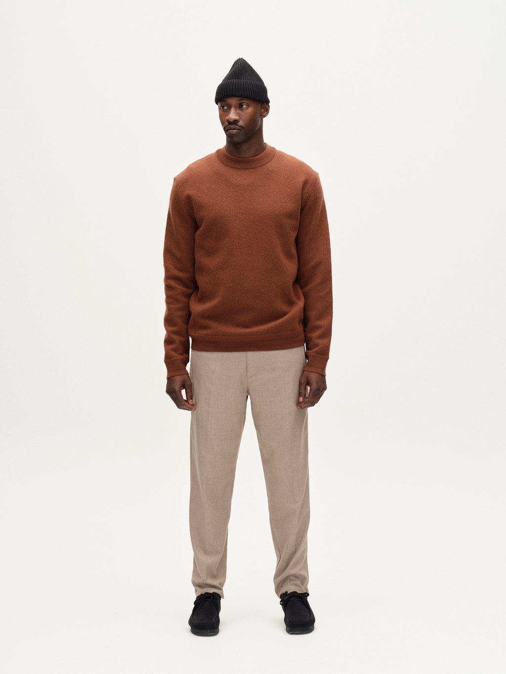 A man stands facing forward, arms at his sides, wearing the Gabba Monza Shafi - Brown sweater with relaxed straight fit brushed cotton pants, a black beanie, and black shoes against a plain white background.