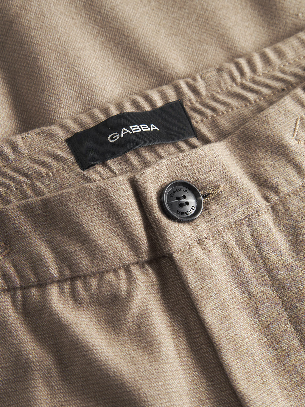 Close-up of Gabba Monza Shafi - Brown brushed cotton pants with a relaxed straight fit, black button, and black GABBA label inside the waistband. The brown fabric is soft, textured, and subtly resembles wool.