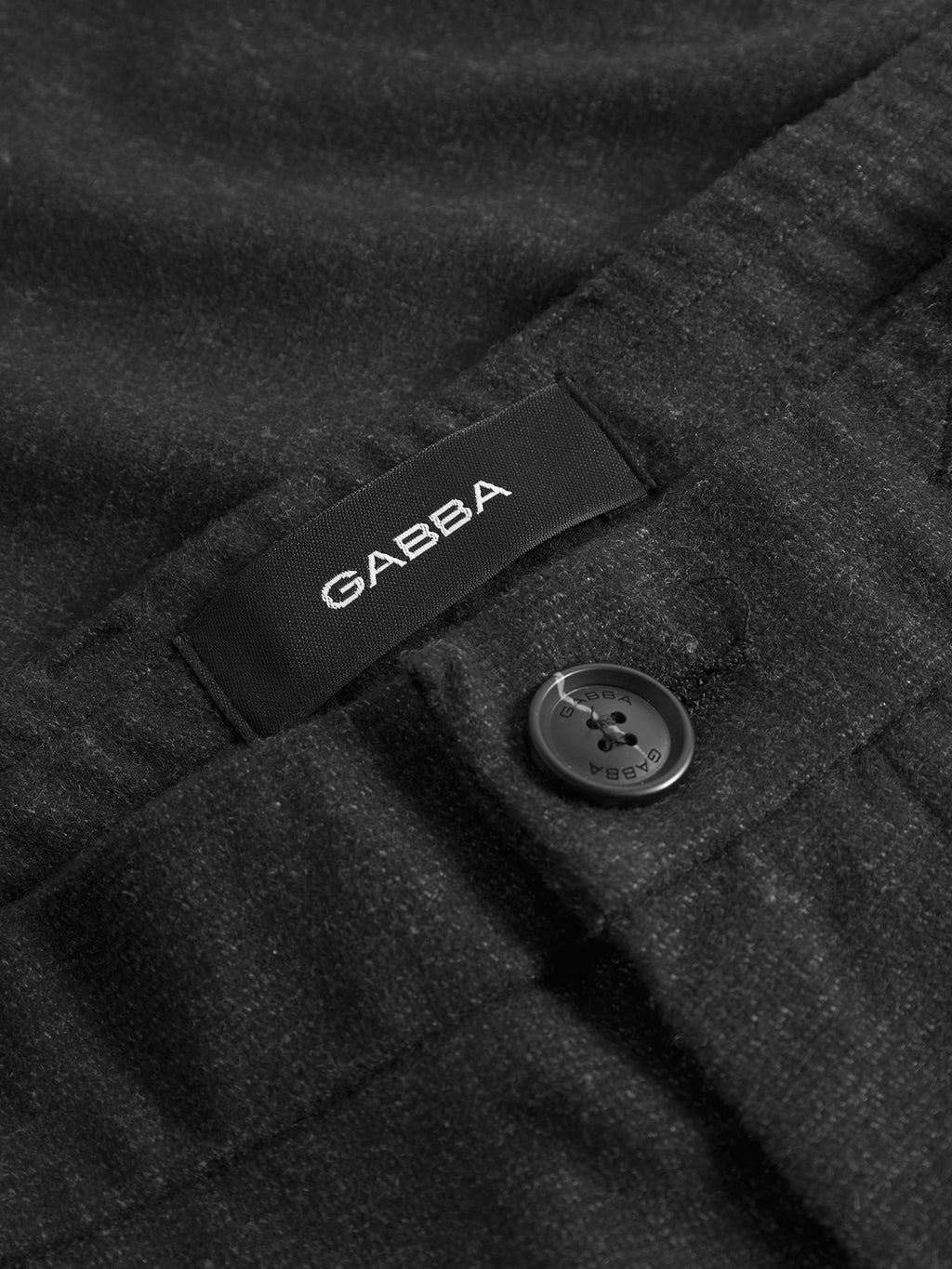 Close-up of Monza Shafi - Black by Gabba, featuring a black four-hole button on textured fabric and the signature label—highlighting the refined details of these premium brushed stretch trousers.