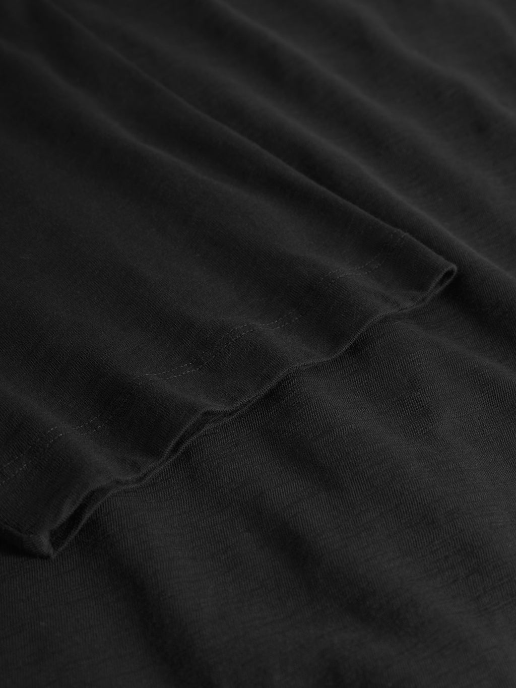 Close-up of Gabbas Pure Ss - Meteorite, showcasing black fabric with a smooth, slightly wavy texture that defines midweight slub jersey. The material looks soft and evenly colored, featuring subtle highlights and shadows for depth.