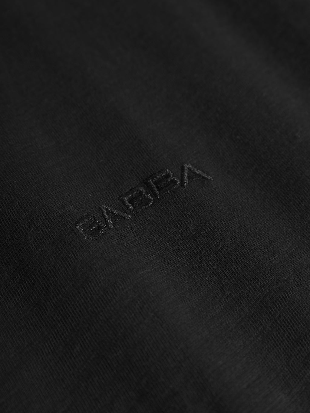 A close-up of a black fabric, similar to the Pure Ss - Meteorite by Gabba, features the word GAISHA subtly embroidered in black thread, giving a minimal and textured look on this midweight slub jersey.
