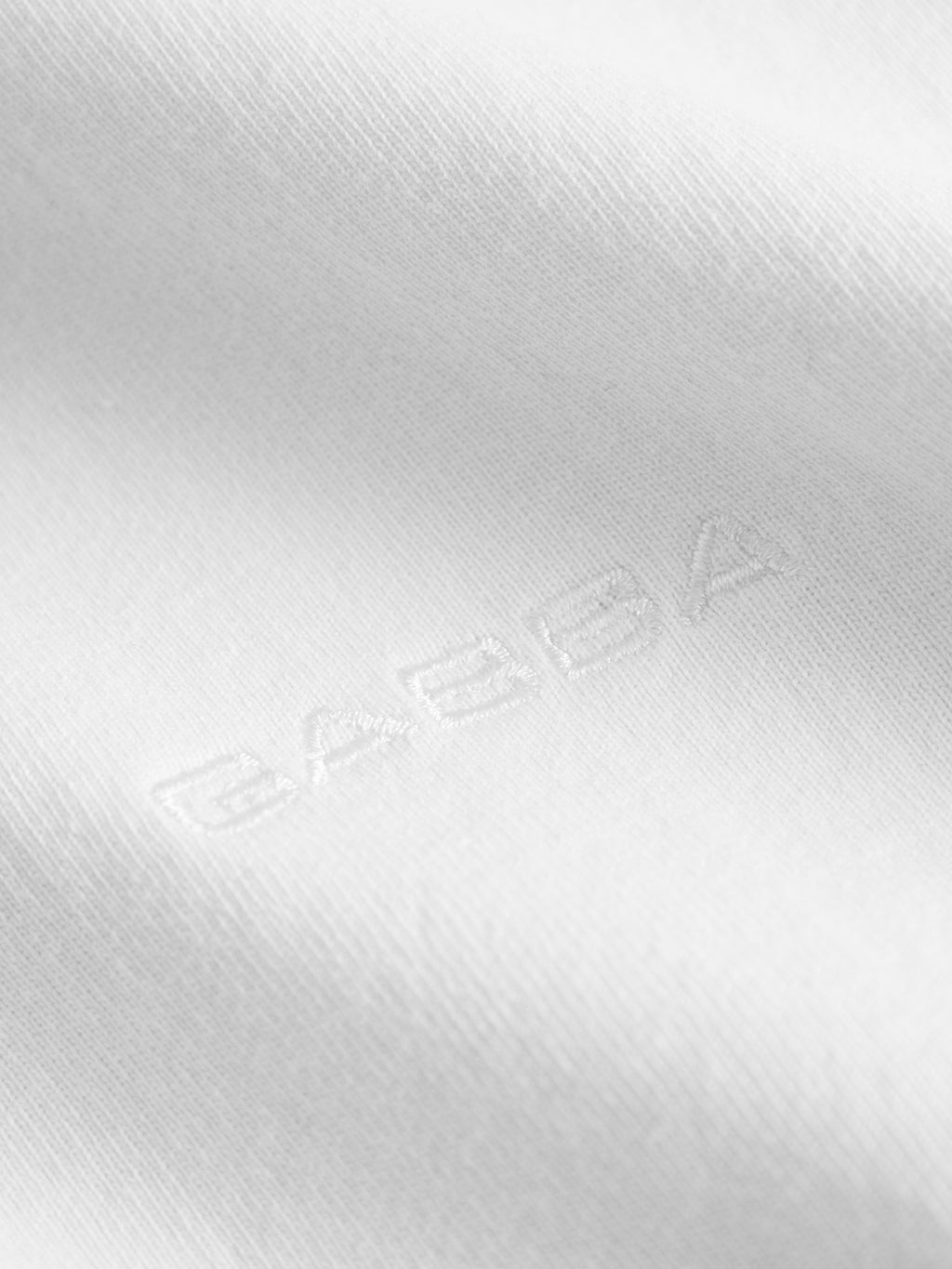 Close-up of the white Nigel Wix Boxy Hour SS t-shirt by Gabba, featuring the brand name subtly embroidered in matching white thread—a refined detail on this modern fit, casual tee.