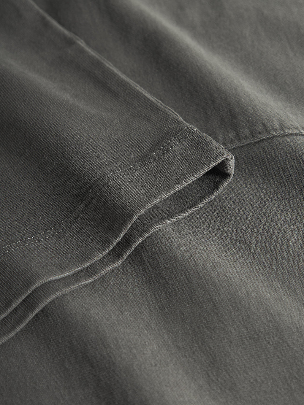 A close-up of the Nigel Wix Boxy Hour SS in dark grey by Gabba shows its visibly stitched, soft, and slightly textured fabric similar to a relaxed fit tee with a folded edge.
