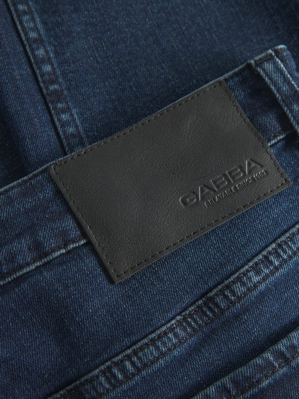 Close-up of dark blue Marc Mego denim jeans by Gabba, highlighting a black leather patch with embossed branding and a slim fit waistband with precise stitching.