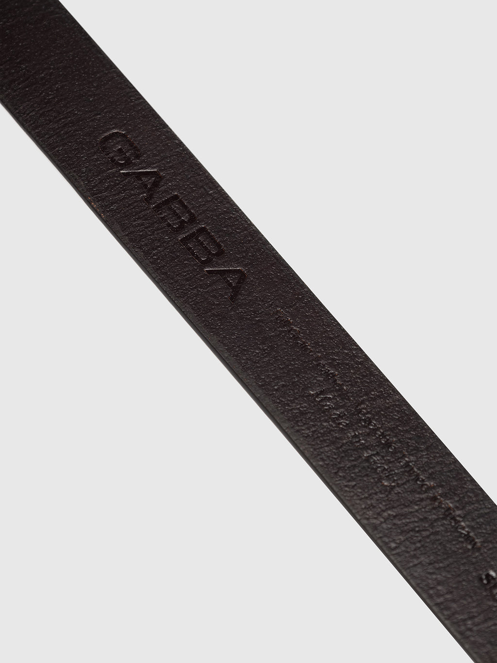 Close-up of an elegant brown leather belt from Gabba. The high-quality texture, displaying a matte finish, is showcased with GABBA embossed on it. Positioned diagonally against a plain light gray background.