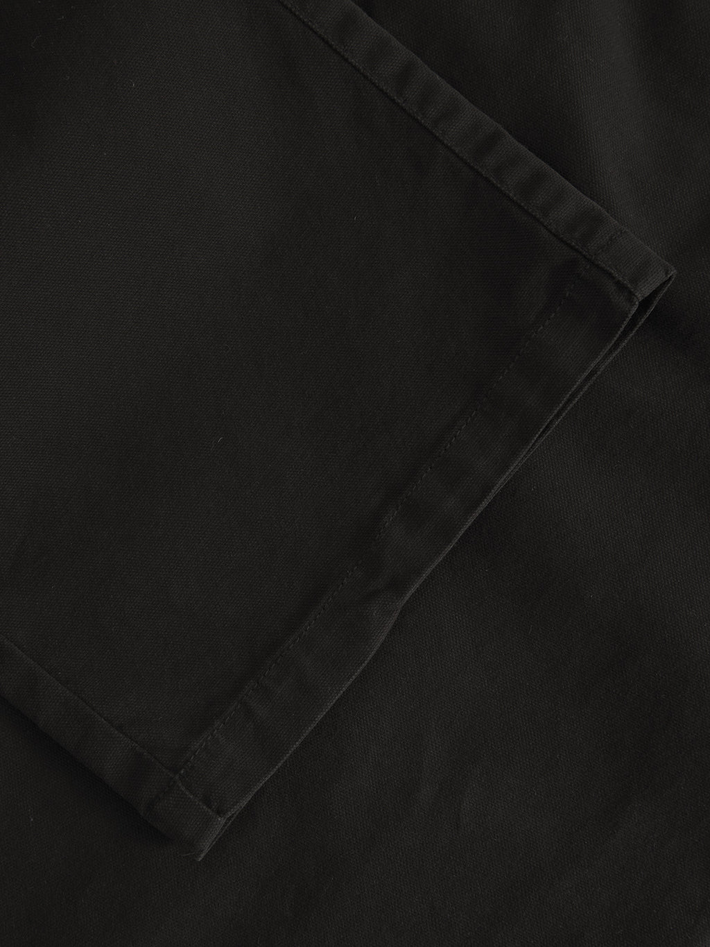 A folded black fabric, Verona Ent - Meteorite by Gabba, showcases visible edge stitching. This durable textured fabric features a matte finish for a sleek and contemporary look.