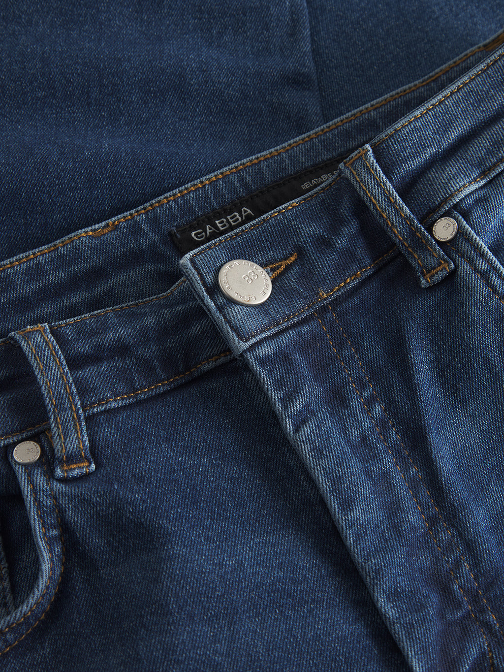 Close-up of Marc K4486 Limited - Mid Blue Denim jeans by Gabba. They feature a modern look with a silver button, visible stitching, a tag inside the waistband displaying the brand name Gabba, and boast classic texture and color for regular fit appeal.