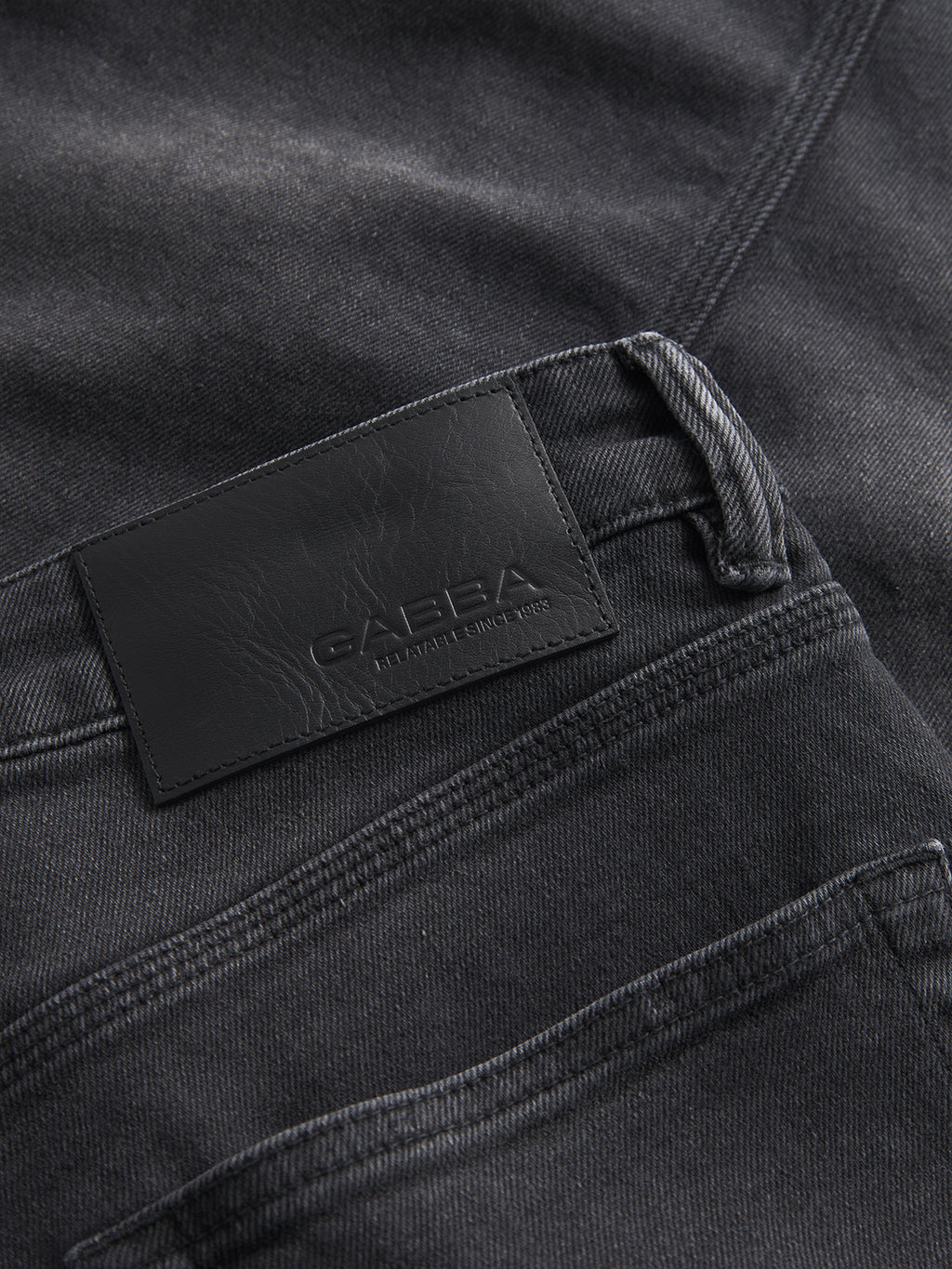 Close-up of Carl K4430 Limited - Grey Denim jeans by Gabba, featuring a black leather patch with embossed text, visible stitching, and belt loops that emphasize their textured look.