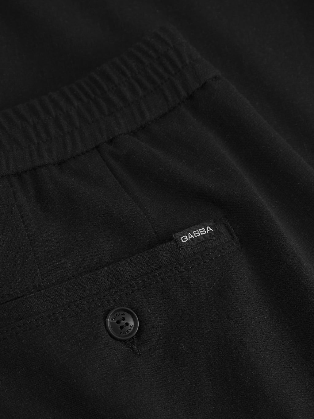 Close-up of Gabbas Napoli 19 Domo Pants in black, featuring an elastic waistband for comfort, a back pocket with a button for classic style, and a small tag labeled GABBA on the pocket.