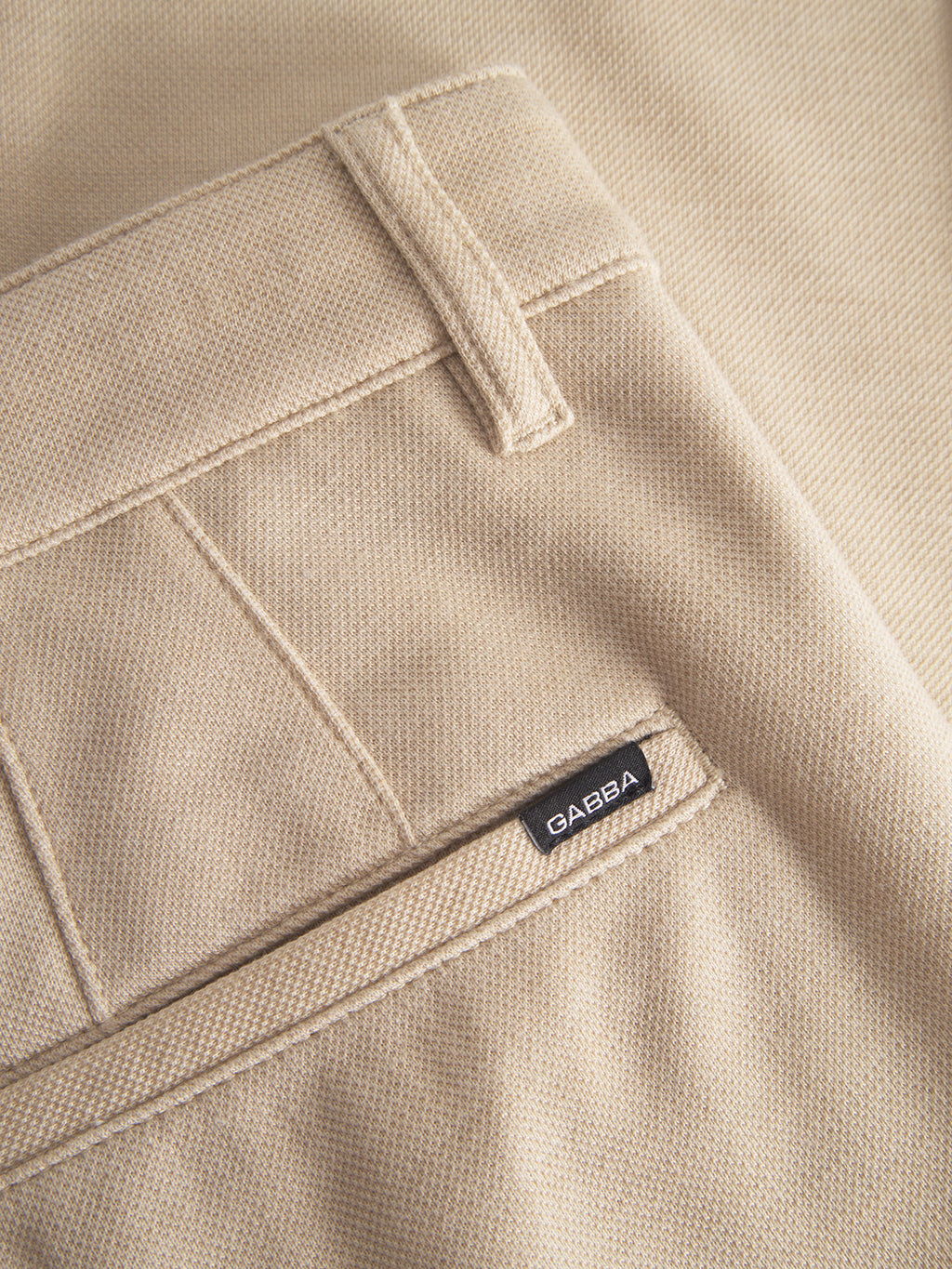 Close-up of the Gabba Venza GKnit - Sand Plaza, beige straight-fitted pants with a back pocket, visible belt loop, and woven label reading Gabba. The classic design is enhanced by innovative structured fabric, showcasing detailed stitching and craftsmanship.