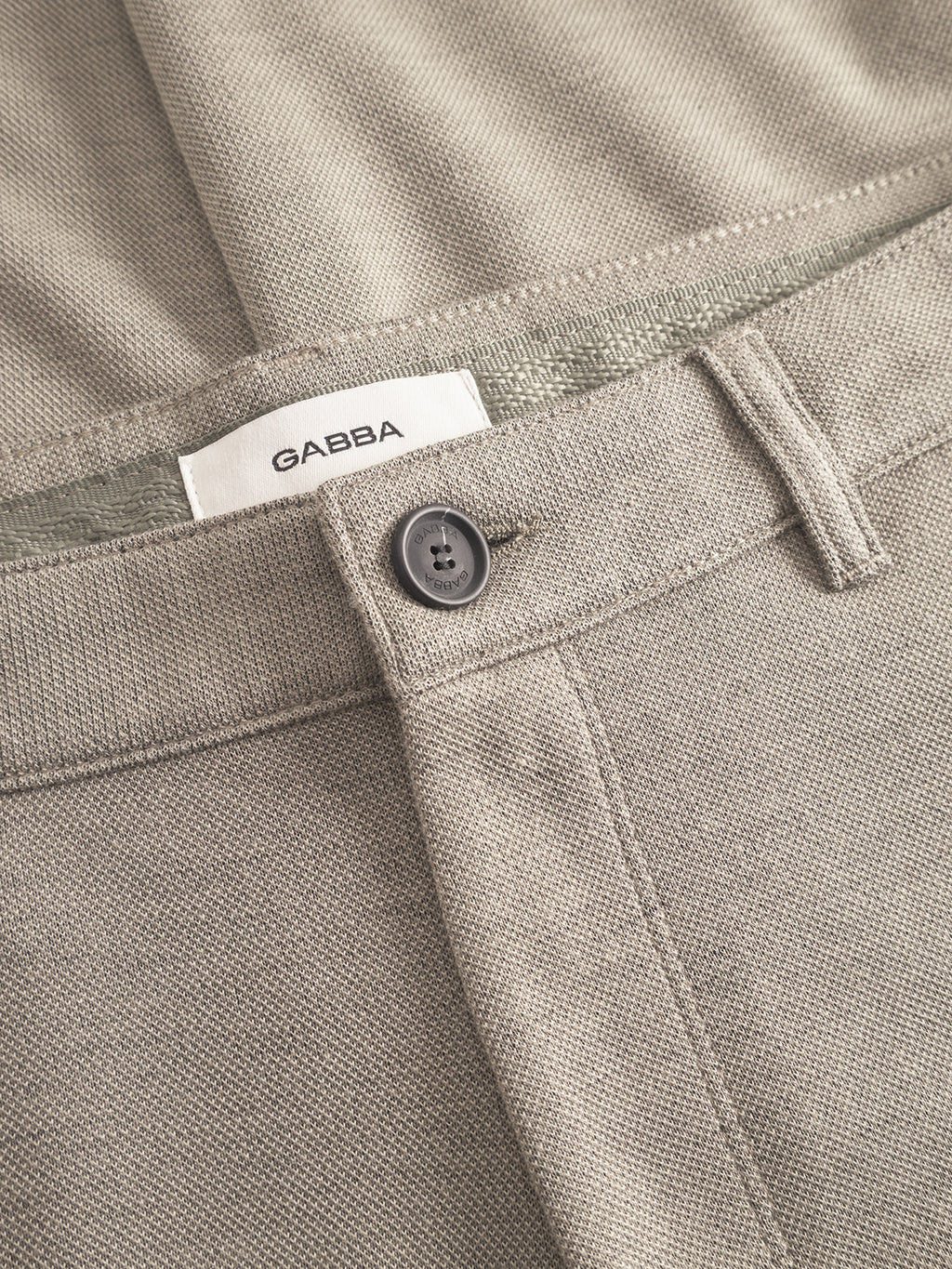 Close-up of Venza GKnit in light green, by Gabba, showcasing the textured structure fabric. Features include a visible black button and belt loop; a white label with GABBA is positioned above the button.