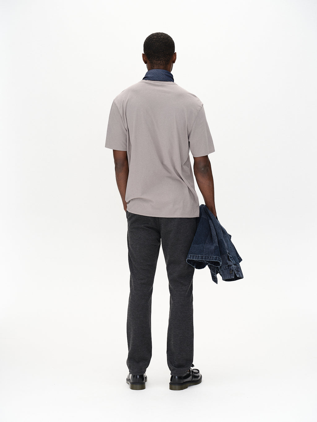 A person, with their back turned, wears the Gabba Venza GKnit in Dk. Grey and straight-fitted pants while holding a denim jacket against a plain white background, showcasing the outfits timeless appeal.