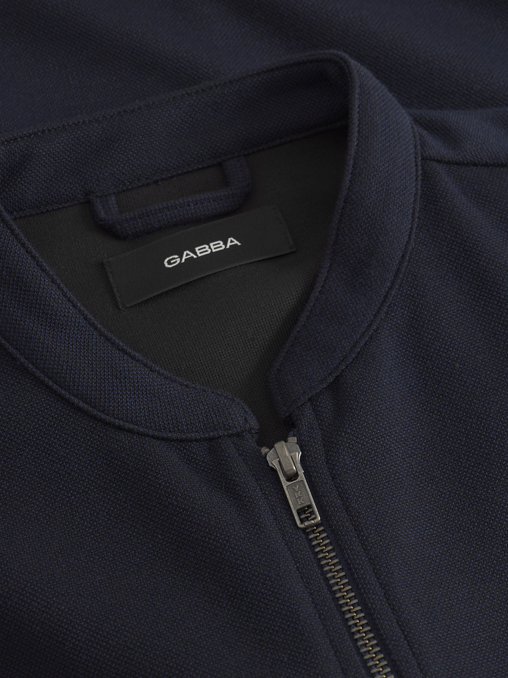 Close-up of Toto Gknit - Navy by Gabba, a perfect everyday dark navy zip-up jacket. Made from a viscose mix with a subtle textured pattern and metal zipper, the black inner label displays the Gabba brand name.