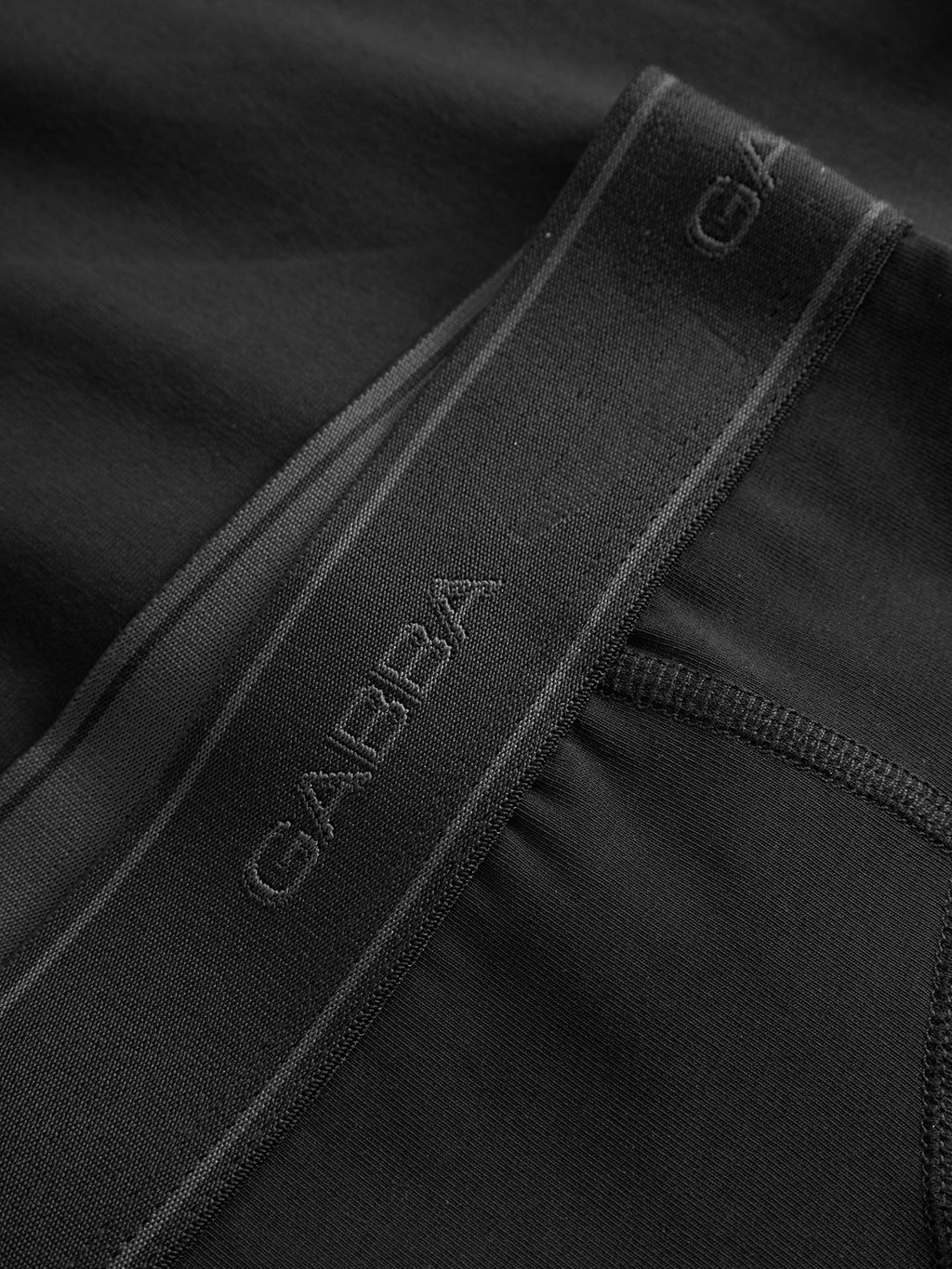 Close-up of smooth black fabric from Gabbas Trunk New - Black, featuring an elastic waistband with the brand logo woven in, highlighting fine stitching and attention to detail.