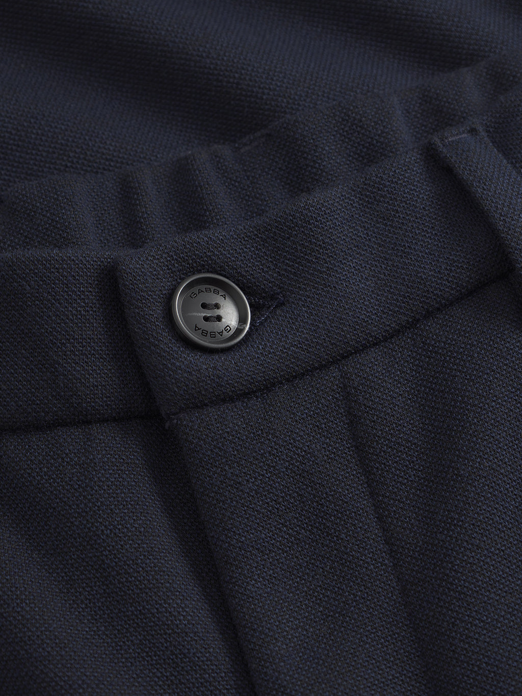 Close-up of dark navy fabric with a metallic four-hole button inscribed C.P. Company. The textured weave knit and elastic waist resemble the comfortable feel of Gabbas Tito GKnit - Navy pants.