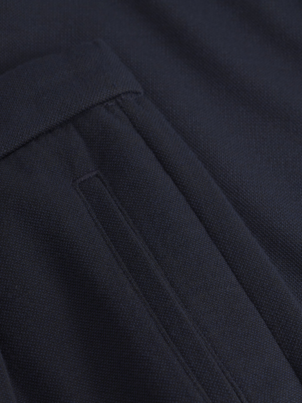Close-up of a dark garment featuring the textured fabric of Tito GKnit - Navy pants by Gabba. The image highlights a pocket with a flap, likely on a suit jacket or coat, emphasizing the intricate knit structure.