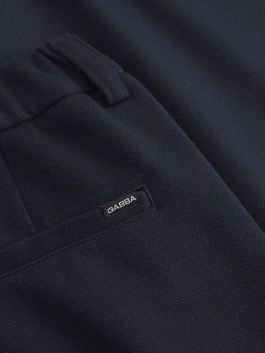 Close-up of the dark navy textured fabric from Gabbas Tito GKnit pants, featuring a neatly stitched structure and a pocket with a slight opening adorned with a black tag labeled Gabba.