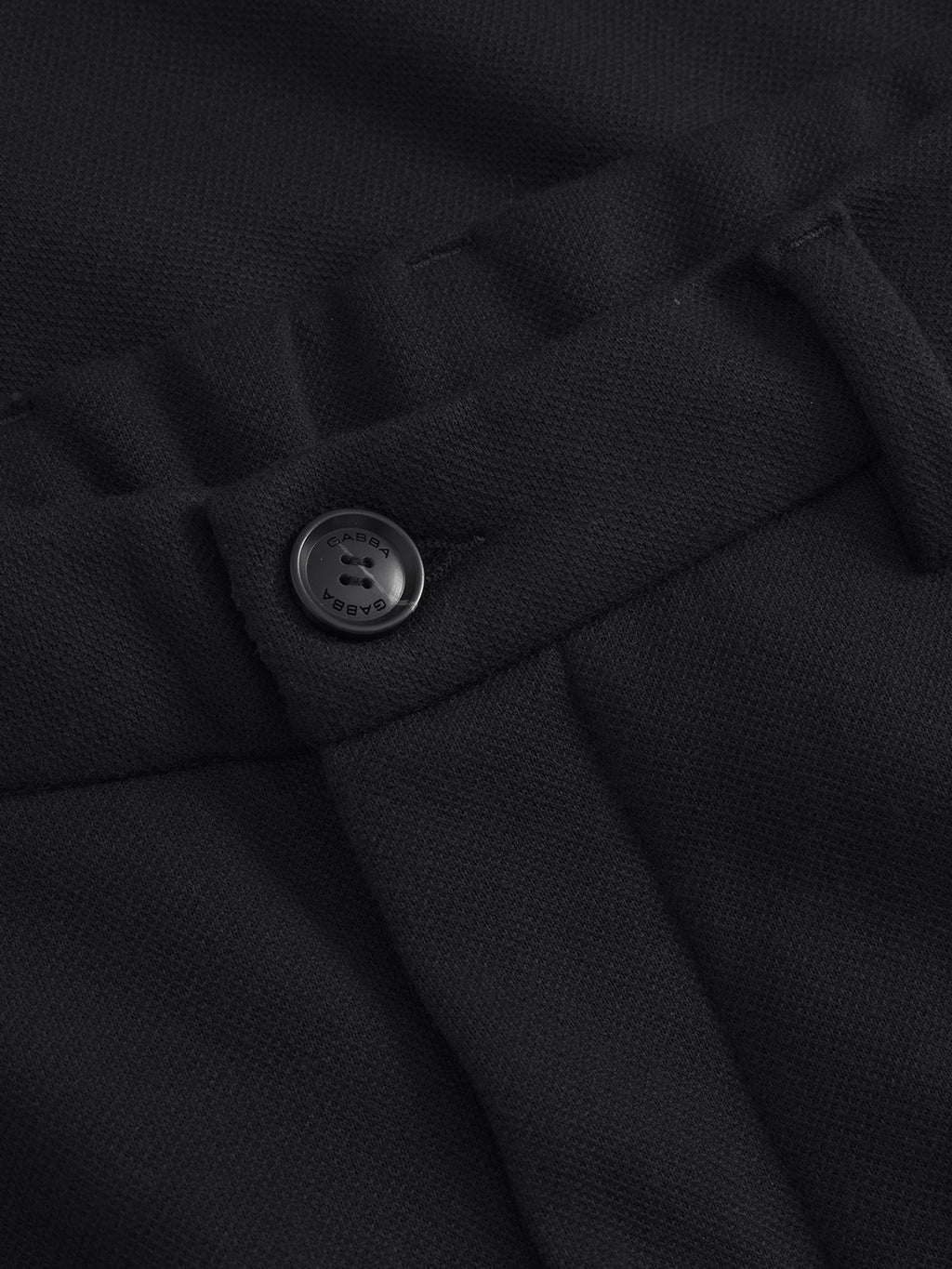 Close-up of the waistband of Gabbas Tito GKnit - Meteorite pants, highlighting the innovative knit structure. A button engraved with Arcane contrasts with the textured fabric, accentuating the belt loop details.