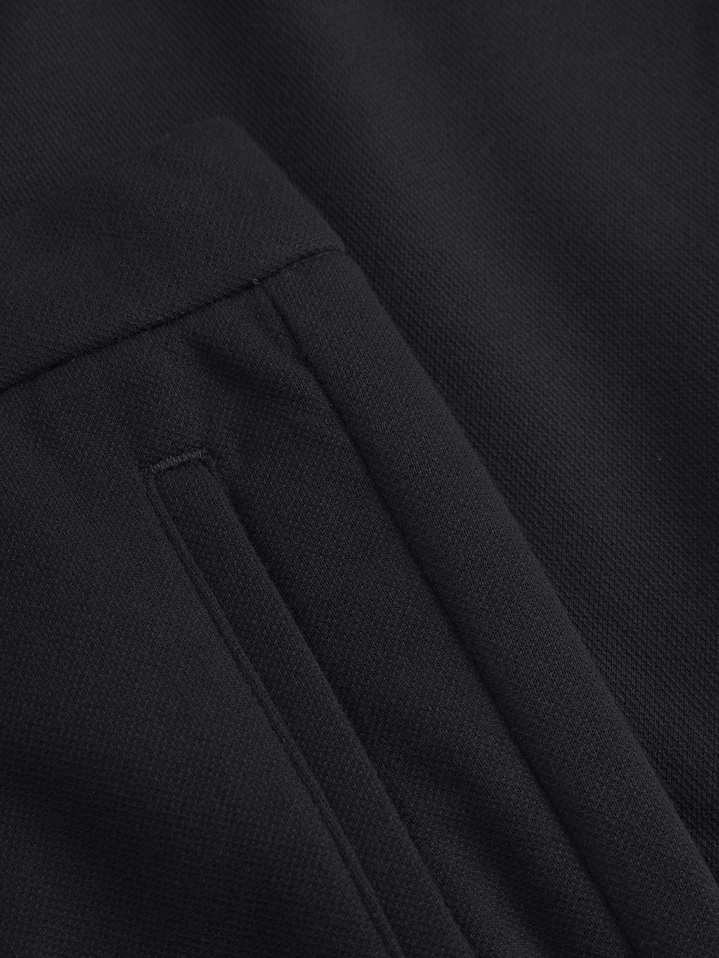 A close-up of the black textured fabric of Gabbas Tito GKnit - Meteorite pants showcases a sleek, minimalist pocket. The innovative knit structure appears smooth and finely woven, accented by subtle edge stitching.