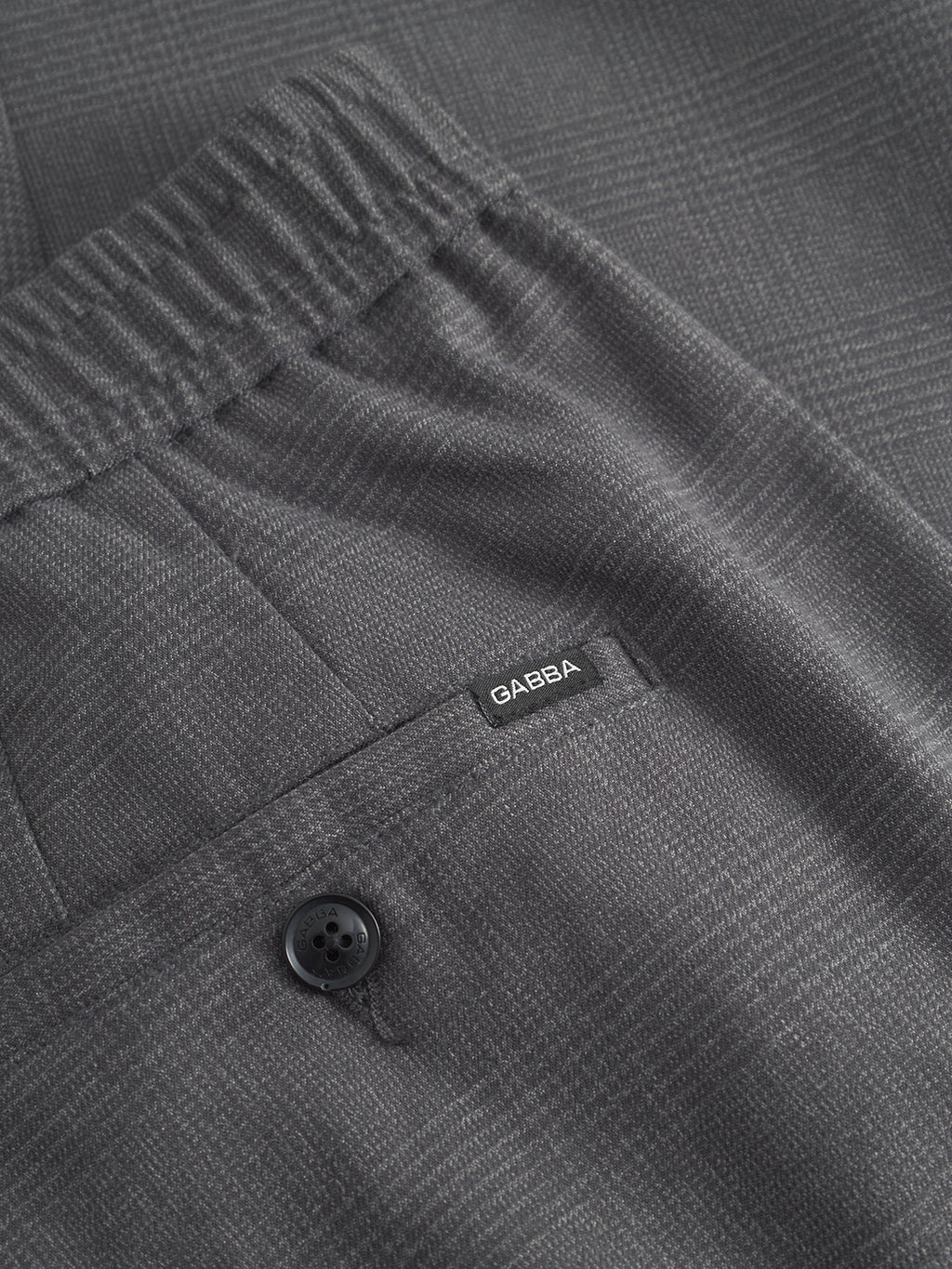 Close-up of Napoli 19 Field Pants in grey by Gabba, featuring a subtle checkered pattern, elastic waistband for comfort, back pocket with a classic black button, and a GABBA label.