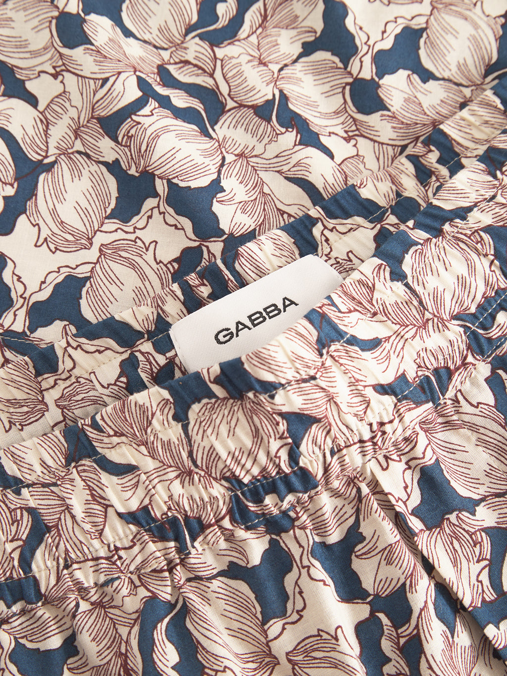Close-up of Porter Epo - Blue Pattern shorts by Gabba, featuring a summer-inspired floral design with red and blue leaves, an elastic waistband, and a white label inside. Made from 100% premium cotton.
