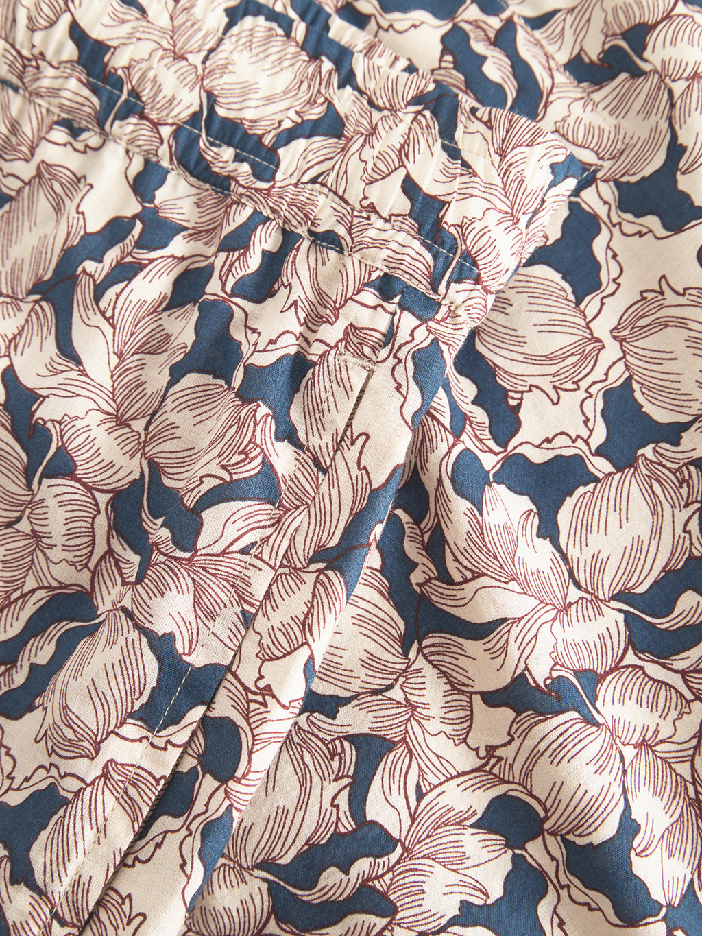 Close-up of a fabric named Porter Epo - Blue Pattern by Gabba, showcasing a cream and navy blue leaf design with red outlines. Made of 100% cotton, its soft texture and visible stitching make it ideal for crafting premium summer-inspired shorts.