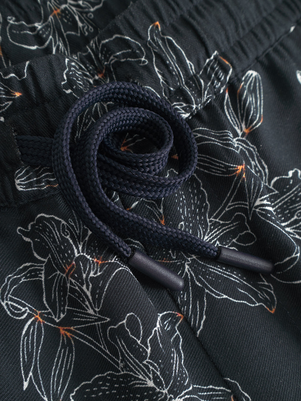 Close-up of Gabba’s Porter Lofi - Flower Mix shorts: black with a white floral print, orange accents, handy pockets, a braided coiled drawstring, and an elastic waistband for comfort.