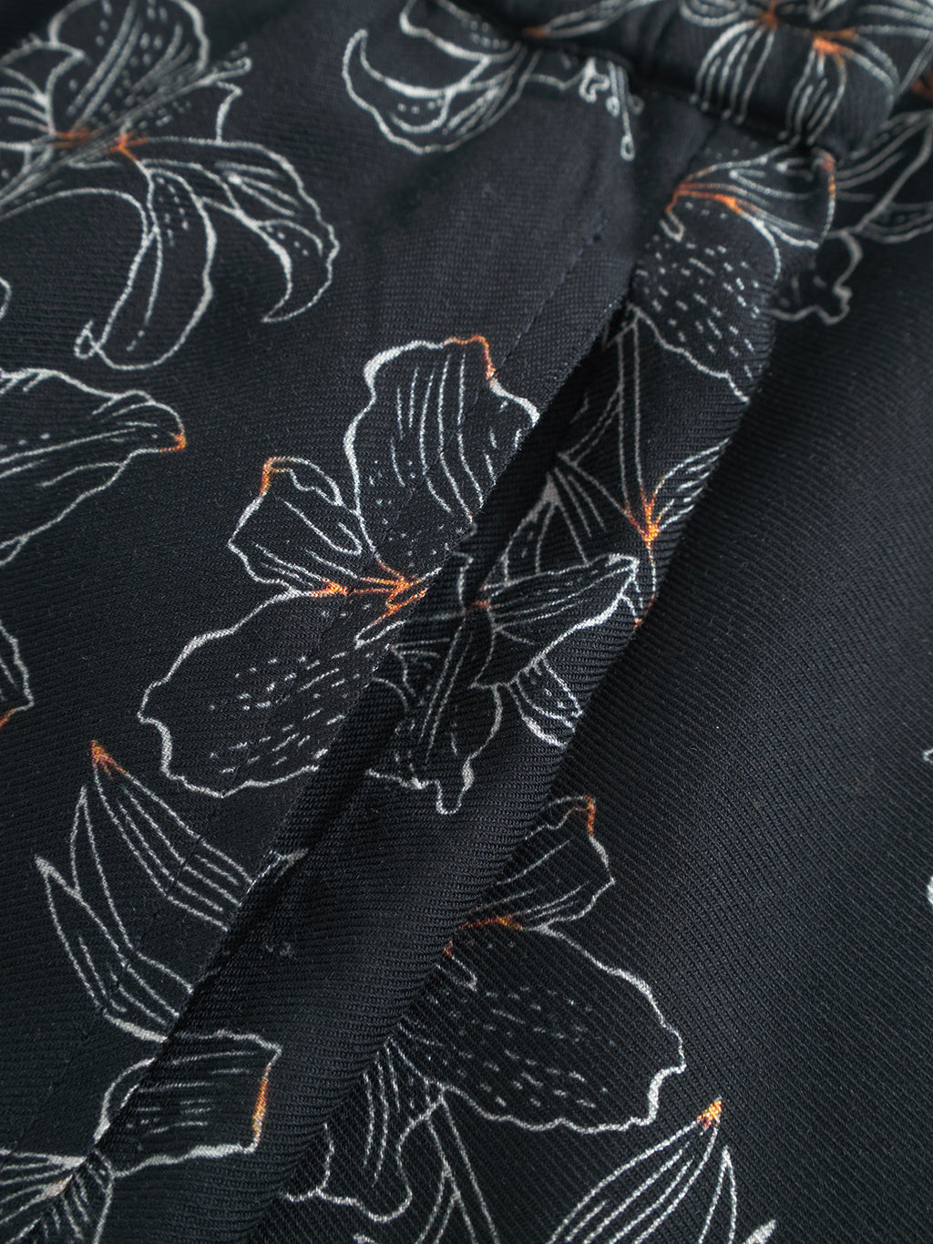 Close-up of Gabba Porter Lofi - Flower Mix shorts in black with a white floral pattern, large outlined flowers and leaves, subtle orange accents on some outlines, and slightly folded fabric.