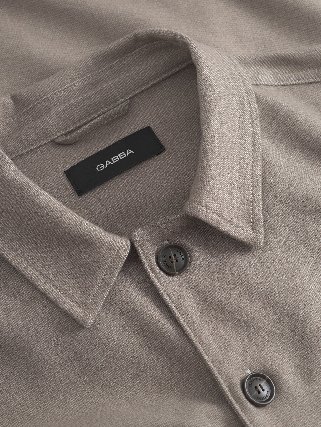 A close-up of the Clipper Shafi - Brown shirt by Gabba showcases elegant stitching and button details. The wool-like fabric offers a soft, textured allure, with the brand label visible inside the collar.