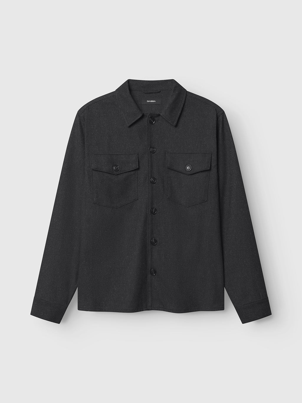 The Clipper Shafi - Black by Gabba is a shirt with a wool-like look, featuring dual buttoned-flap chest pockets, a collar, and long sleeves, set against a plain light gray backdrop.