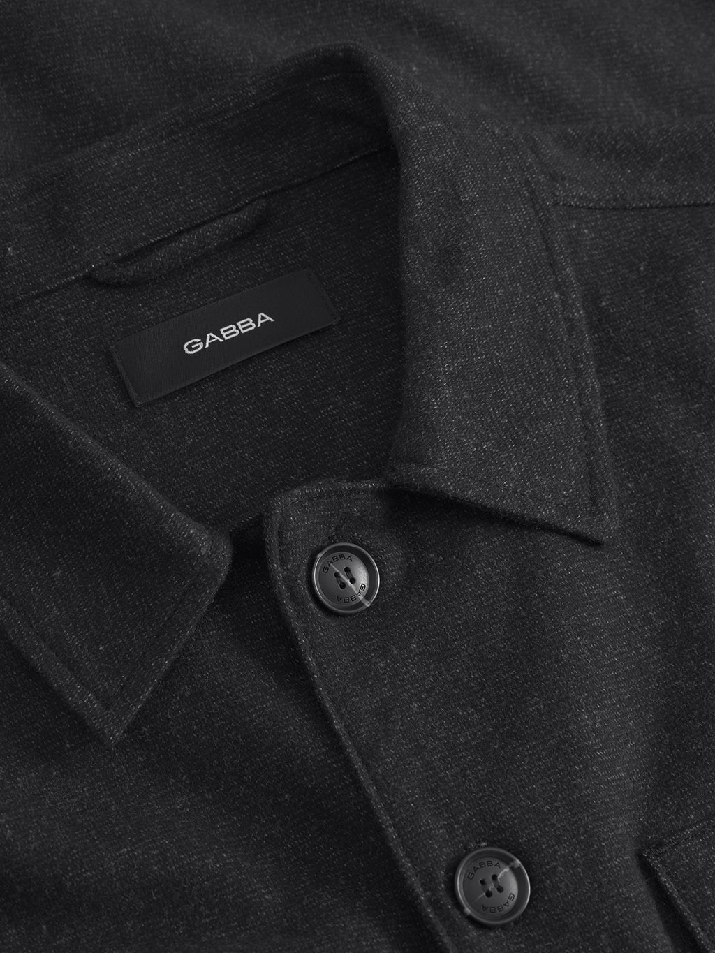 Close-up of a dark gray Clipper Shafi - Black shirt from Gabba, featuring buttons and a pointed collar. It has a wool-like texture with dual chest pockets and a soft pattern, visible label inside the collar.