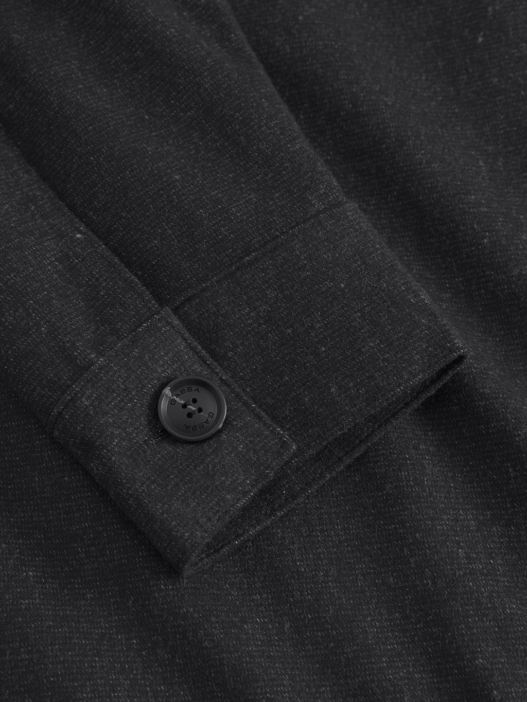 A detailed view of textured, dark fabric on the Clipper Shafi - Black from Gabba shows a wool-like texture with speckles and a black button sewn onto the cuff.