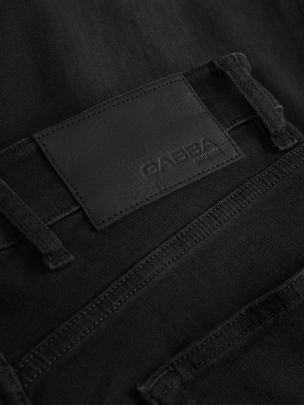 Close-up of the waistband and back pocket of Alex Telsa - Black Denim jeans by Gabba, showing a black leather patch with the embossed brand name and worker-cut waistbands for a trend-focused style.