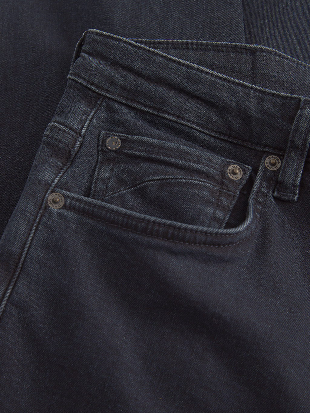 A close-up of Marc Panter - Dark Blue Denim by Gabba shows the front pocket and belt loops, with a slightly worn fabric that highlights texture and stitching. These classic fit jeans are laid flat on a matching dark background.