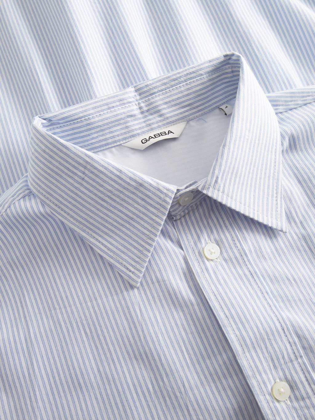 Close-up of the Gabba Sven Reg. Form LS shirt in white stripe, featuring premium yarn-dyed stripes in light blue and white, a neatly folded collar with an inside tag, and a button-down style. The 100% cotton fabric is crisp and well-ironed, highlighting its classic formal design.
